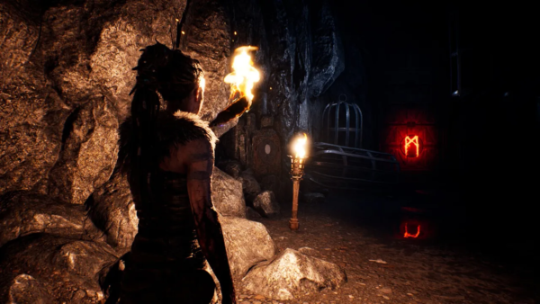 Сенуа из Hellblade держит факел в пещере